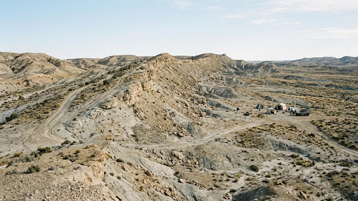 Vista amplia del desierto de prueba con una ladera extrema y un pequeño rover de ensayo lejos del plano principal, en un entorno científico realista.