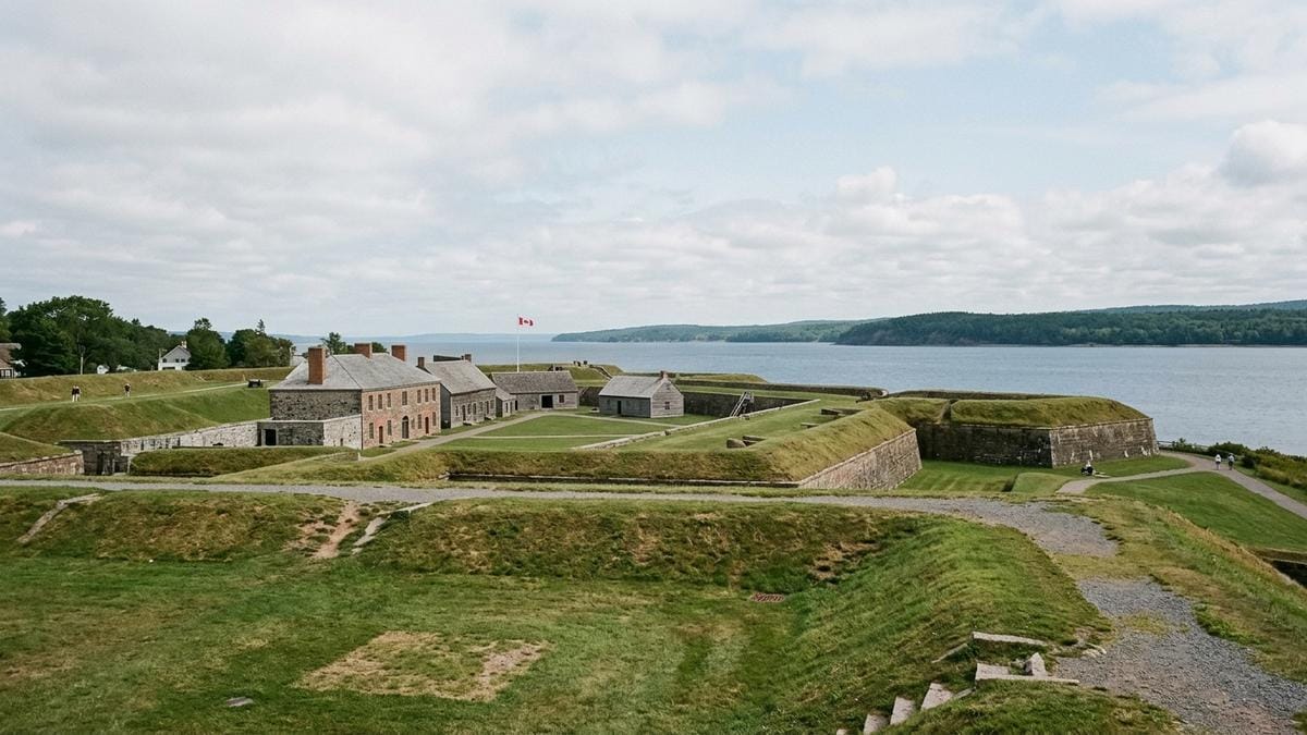 Vista lateral de un fuerte histórico en Nueva Escocia junto a la costa atlántica, con muros de piedra, hierba baja y cielo nublado suave.