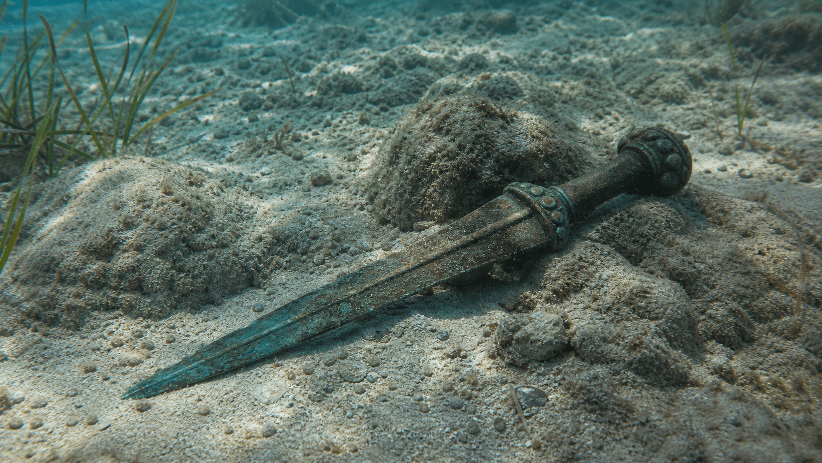 Recreación editorial de una espada de bronce en un fondo marino poco profundo