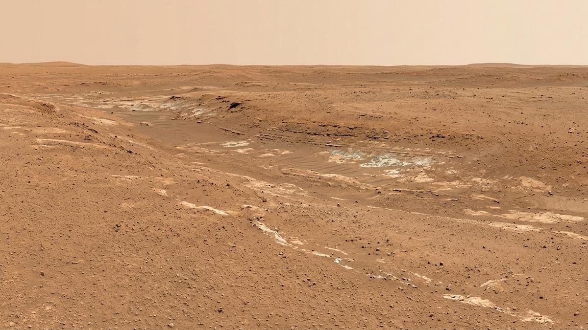 Paisaje amplio de Utopia Planitia con una depresión suave y estratos minerales claros bajo un cielo tenue.