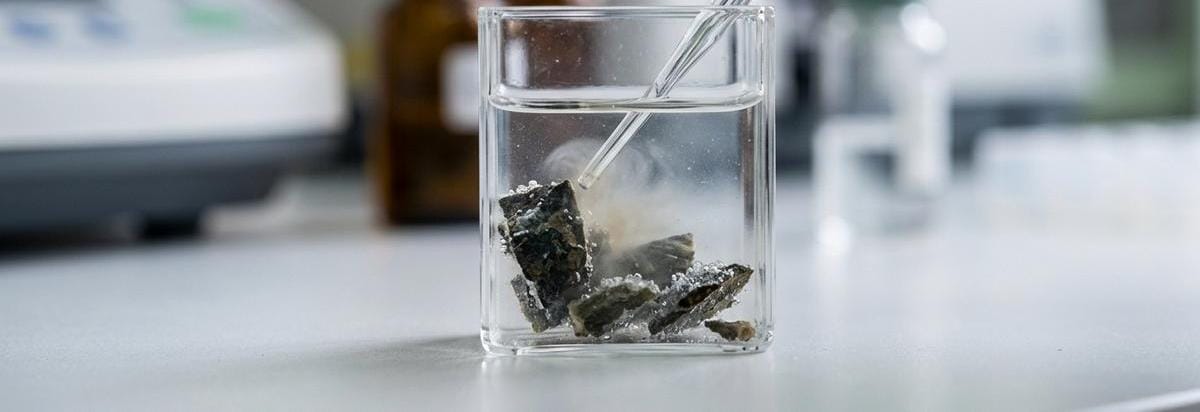 Detalle de una muestra mineral en placa de análisis con precipitados y un gotero en laboratorio