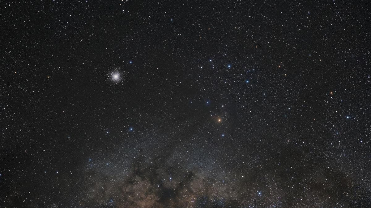 Campo estelar amplio con un cúmulo globular lejano y tenue, junto al entorno de la Vía Láctea, en una composición editorial de apoyo.