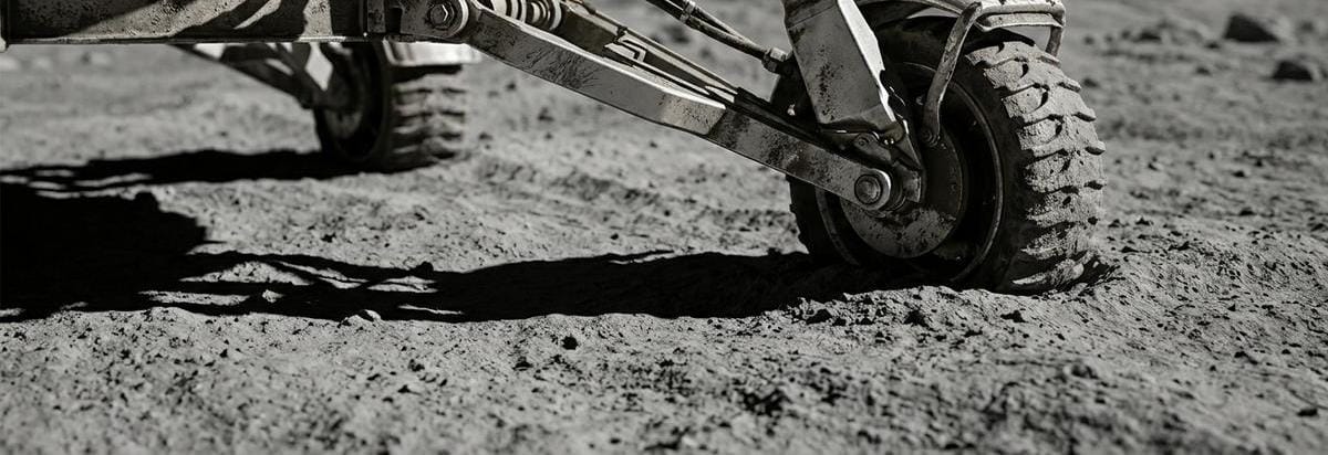 Detalle técnico de una rueda y sensores de un rover o módulo de pruebas sobre regolito lunar, con polvo fino, sombras duras y herramientas de inspección.