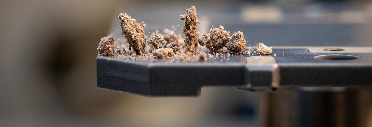 Detalle macro de granos de polvo marciano flotando cerca de una superficie de sensor, con destellos electrostáticos sutiles y enfoque técnico.