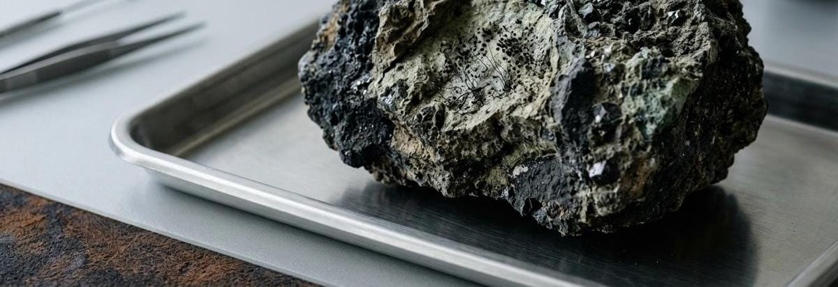 Macro de una muestra mineral volcánica con esporas o estructuras microscópicas sugeridas de forma sutil, junto a instrumentos de laboratorio discretos, para transmitir análisis y cautela científica.