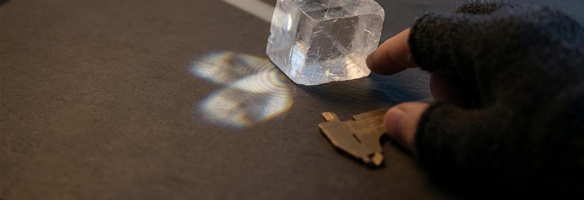 Detalle técnico de un cristal de espato de Islandia alineado con un patrón de luz polarizada sobre un fondo oscuro de estudio.